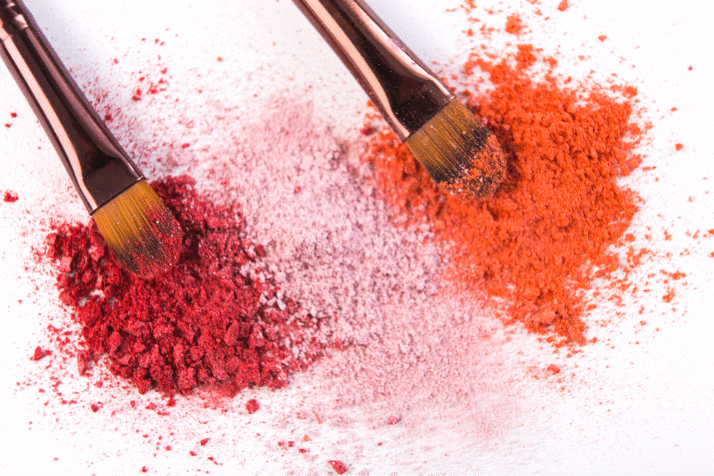 Bold red and orange makeup powders with brushes on a bright background.