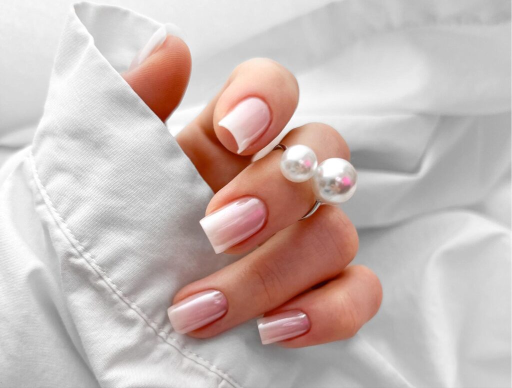 Elegant pink nail design featuring pearl accents on a soft white backdrop.