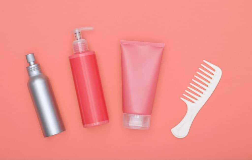 Essential hair care products and a comb on a coral background.