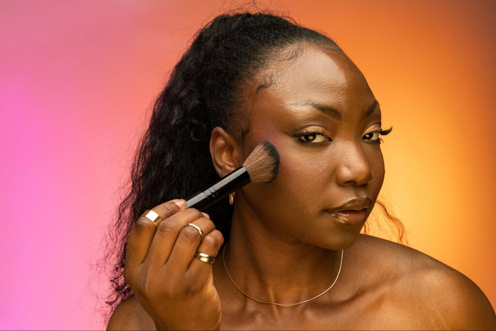 Woman applying vibrant makeup, achieving a flawless beauty look against a colorful background.