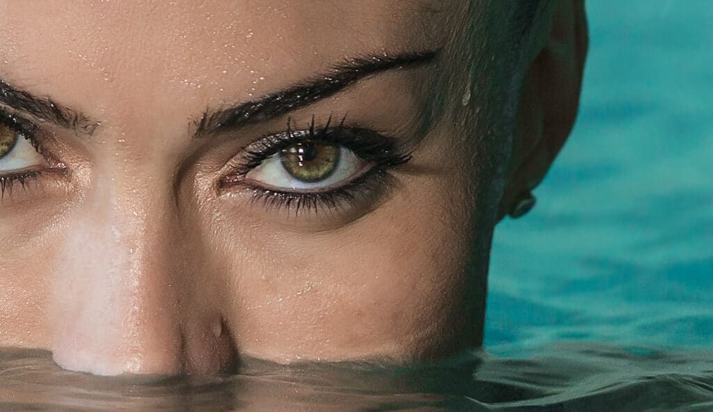 Captivating eyes emerge from sparkling water, embodying beauty and grace by the poolside.