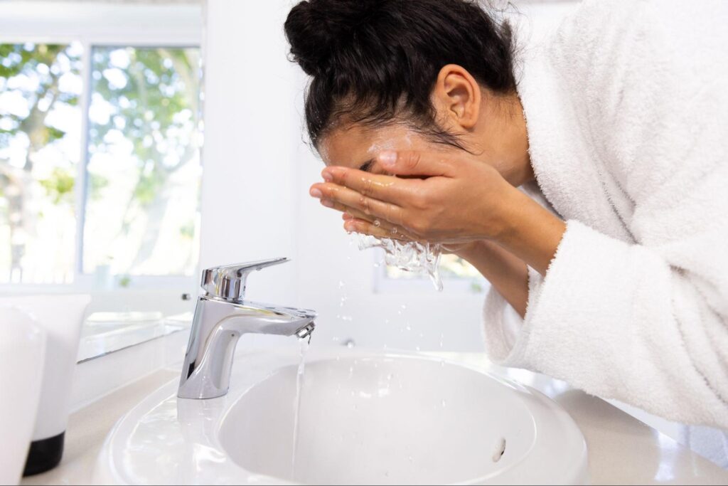 Woman refreshing her skin with a morning face wash at the sink.